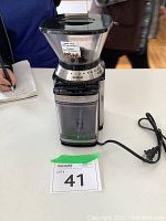 Front view of chrome plated Cuisinart coffee grinder with bean hopper, grind selector dial, cup slide dial, and power cord.