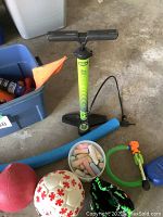Photo showing green and black Bell bicycle floor pump, white bowl with colorful sidewalk chalk, red ball, white soccer ball with red maple leaves, black catcher's mitt, foam pool noodle, and green air rocket launcher