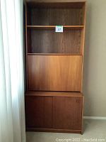 Front view of the modular teak wall unit showing open shelving, fold-down panel door middle section, and lower cabinet door.