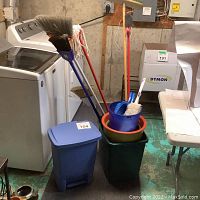 Photo shows washing machine and dryer in background with cleaning tools including broom, mop, buckets, and trash bin in foreground arranged for sale.