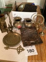 Photo of brass and terracotta ethnic decor items including vases, plates, figurines, and embossed metal plates arranged on a table.