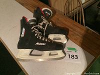 Pair of black Micron ice skates with white blades, size 12, on table.