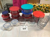 Multiple glass storage bowls with a variety of colored plastic lids, stacked and separate on a table.