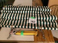 Folded green and white striped fabric hammock with yellow straps placed on a wooden table.