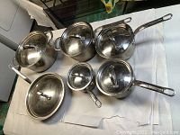 Full view of Lagostina pot set including large pots, saucepans, frying pan, all with lids, displayed on a white surface.