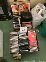Full view of lot showing stacks of vinyl records, multiple CD cases, and a white plastic bag likely with more CDs or DVDs.