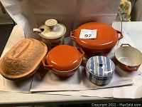 Photo of six covered bakeware pots including glazed metal, ceramic, and clay pieces arranged on a white paper