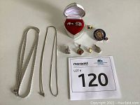Photo showing two silver chains, four pendants, two rings in silver heart-shaped box, and enamel pins with MaxSold lot number card.