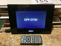 Sony DPF-D720 digital photo frame powered on with model number displayed, with Sony remote control in front