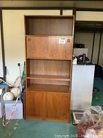 Full front view of the first teak wall unit showing upper closed storage, middle open shelf, and lower sliding doors with hidden pull out drawers and open compartment.