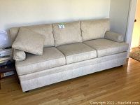 Full view of beige Thomasville 3 seater couch showing three seat cushions, three back cushions, one cushion slightly askew, and slipcovered arms.