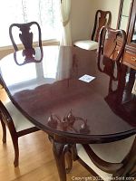 Cherry finish oval table top reflecting chandelier, partial view of chairs