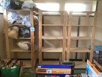 Photo shows three wooden shelving units positioned side by side with some items on and around them removed. Shelves are made of natural wood with four shelf levels each.
