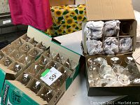 Boxes of assorted clear wine glasses arranged in packaging, some glasses wrapped in paper for protection