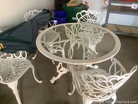 Full view of round glass top table, four wrought iron chairs and folded umbrella