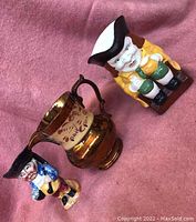 Top view of three ceramic jugs showing the Toby character jugs and the copper lustre jug on a pink fabric background