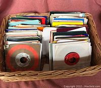 Wicker basket filled with vertically stored 45 RPM vinyl records in various colored paper sleeves, showing the diversity and quantity of the collection.