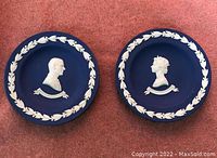 Front view of two blue Wedgwood Jasperware plates with white relief profiles of Queen Elizabeth II and Prince Philip, each with laurel wreath border.