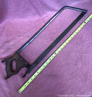 Full view of the antique butcher's saw laid flat with measuring tape beside it showing approximately 20 inch length.