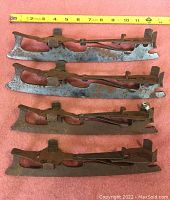 Four metal antique ice skates laid out horizontally with measuring tape above showing about 11.5 inches in blade length