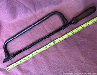 Full view of the antique hacksaw next to a tape measure showing length approximately 21 inches.