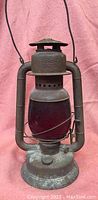 Front view of vintage GSW Beacon windproof lantern with red globe showing metal frame, globe and handle.