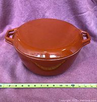 Top view of the round brown enamelled cast iron cook pot with lid and handles, showing size scale with tape measure.