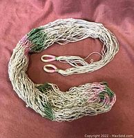 Folded double hammock showing intertwined cotton strings with green and pink accents and two looped hanging ends on a rose-colored fabric background.