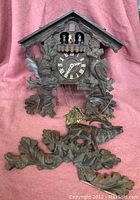 Full front view of wooden German cuckoo clock showing carvings, dial and separated decorative pieces