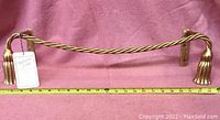 Front view of gilt towel bar lying horizontally on pink fabric with a measuring ruler beneath showing about 18 inches long.