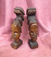 Front and side view of two wooden hand carved Afro inspired bookends with wire decorations set on pink cloth background.