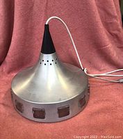 Full view of the aluminum conical hanging lamp with white electrical cord on red fabric background