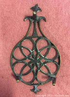 Top view of fine cast brass trivet showing intricate pierced pattern and scroll detailed handle, placed on a red fabric background
