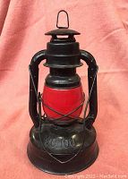 Front view of a Dietz No 100 RR hurricane lantern showing black metal frame and red globe with No 100 marking on base.