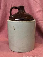 Front view of the large jug crock showing the two-tone coloring with a matte light stoneware bottom and glossy dark brown glazed neck and handle.