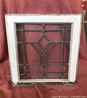 Front view of leaded glass window showing geometric lead design and white wooden frame with wear.
