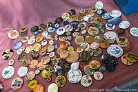 Photo showing a large assortment of pin back buttons spread out on a pink cloth, featuring various logos, themes and colors.