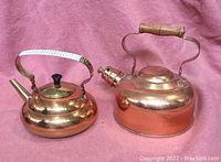 Photo of two shiny copper kettles on pink background, showing metal and wooden handles and spouts.