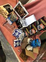 Photo showing NOMA Marquee string lights boxes, puzzles, glass bottles, ceramic mugs, candles, dummy security camera box.