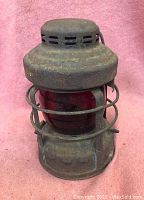 Front view of the vintage railroad lamp showing the metal top ventilation and protective cage around the red globe.