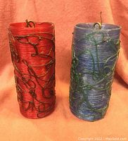 Front view of two cylindrical light shades, one red and one blue, with wrapped metal wire decorations on surface.