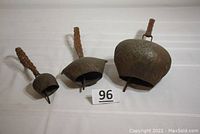 Front angled view of the three metal primitive animal bells with woven straps, showing size difference and metal patina.