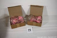 Two open cardboard boxes containing multiple individually wrapped pink flamingo decorations.