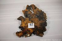 Front view of the driftwood wall clock showing irregular live edge, thick lacquer finish, Roman numeral clock face with gold numerals and white hands.
