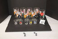 Full set of eight drinking glasses, five shot glasses, and six 8-ball swivel sticks displayed on black mat, numbered '37' card present