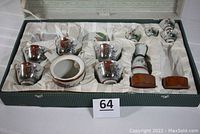 Open box showing hand-painted Japanese porcelain pieces inside with padding, including teapot, teacups, sake flagon and cups