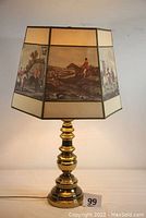 Full view of brass electric lamp with hexagonal paper shade showing horse scenes in painted panels, lamp off, front angle