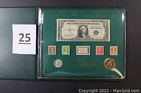 Front of display case showing 1935 $1 Silver Certificate, five stamps, a 1976 Bicentennial Quarter, and a gold-colored commemorative medallion.