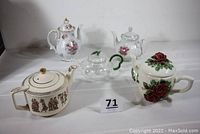 Five teapots arranged on white surface showing diverse styles and materials in the lot.