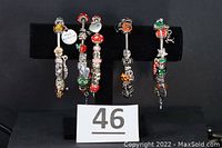 Five charm bracelets displayed on a black stand, showing their distinct seasonal themes in red, silver, green, orange colors.